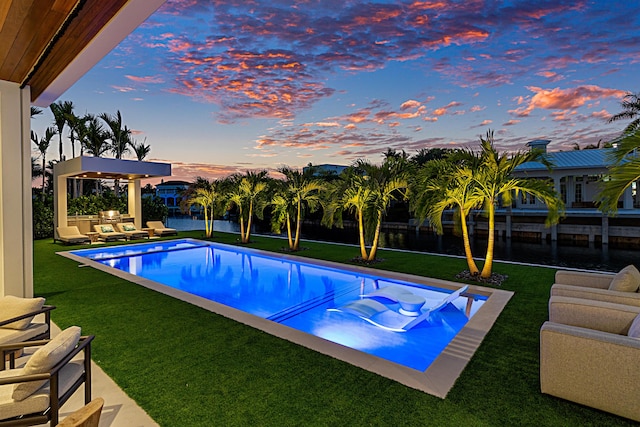 pool at dusk featuring a patio area, an outdoor pool, and a lawn