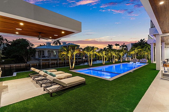 pool at dusk with an outdoor pool, a patio, ceiling fan, a yard, and an outdoor living space