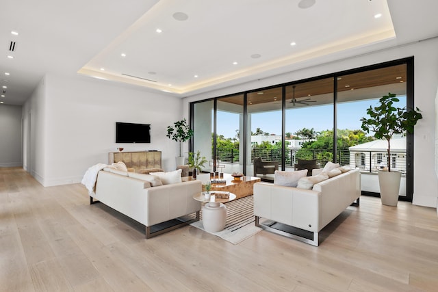 living area featuring light wood finished floors, a tray ceiling, recessed lighting, and baseboards