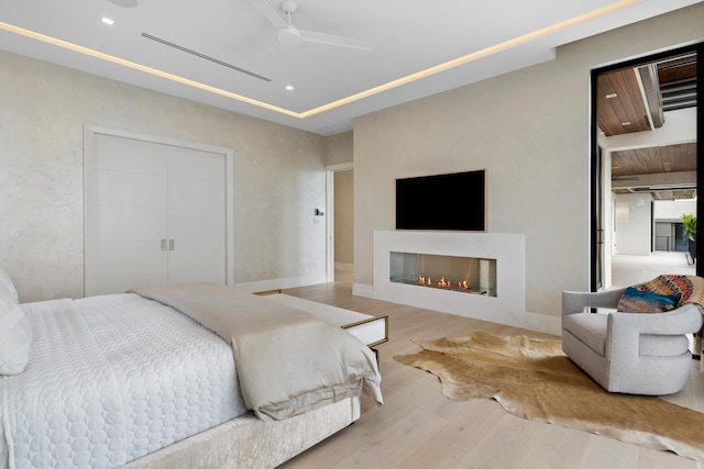 bedroom with baseboards, a glass covered fireplace, ceiling fan, wood finished floors, and recessed lighting