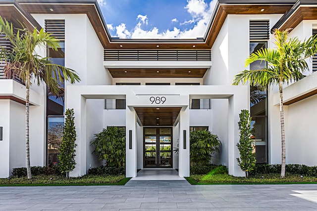 doorway to property featuring a balcony, french doors, and stucco siding