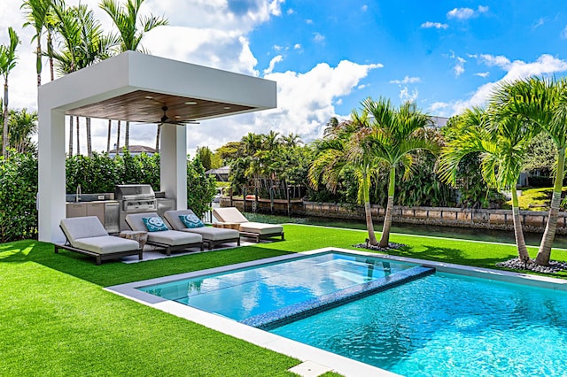 view of swimming pool with an outdoor kitchen, a lawn, ceiling fan, grilling area, and a sink