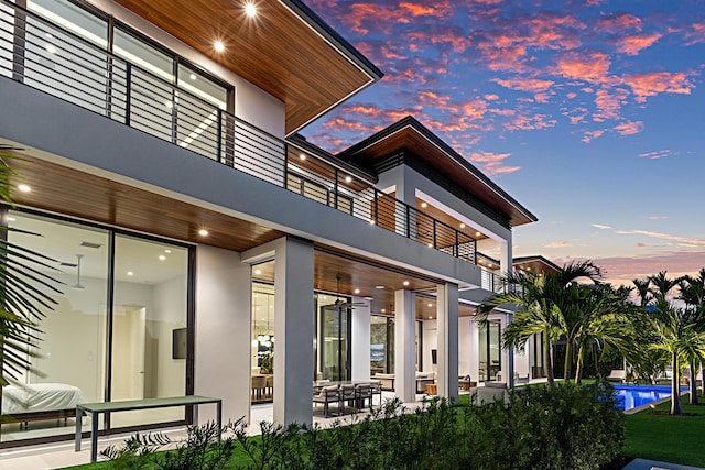 back of property at dusk featuring an outdoor pool and stucco siding