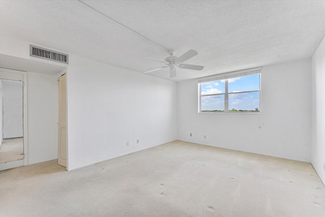 empty room featuring a textured ceiling, ceiling fan, carpet, and visible vents