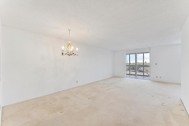 spare room with light carpet, an inviting chandelier, and a textured ceiling