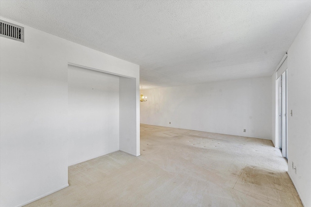 unfurnished room featuring an inviting chandelier, visible vents, a textured ceiling, and carpet flooring