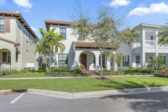 mediterranean / spanish house with stucco siding, a tile roof, a front lawn, and uncovered parking