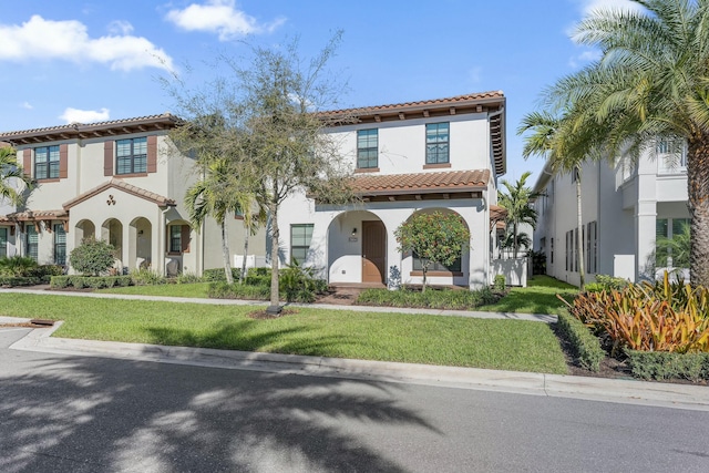 mediterranean / spanish-style house with a front lawn, a tiled roof, and stucco siding