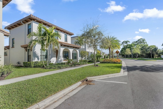 view of front of property with stucco siding, a tile roof, a front lawn, and uncovered parking