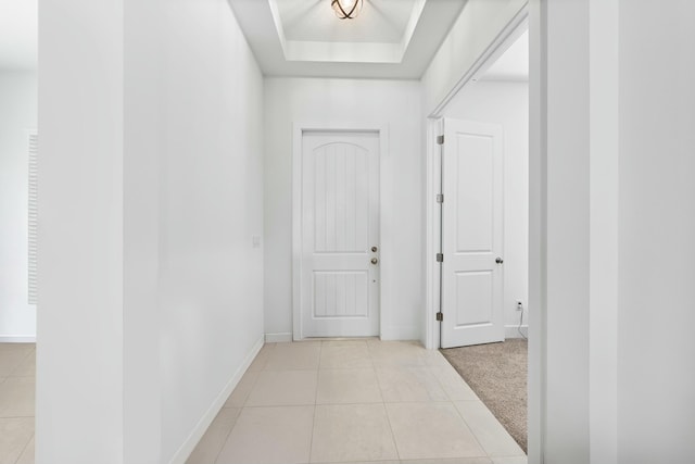 hallway with light tile patterned floors, light carpet, a raised ceiling, and baseboards