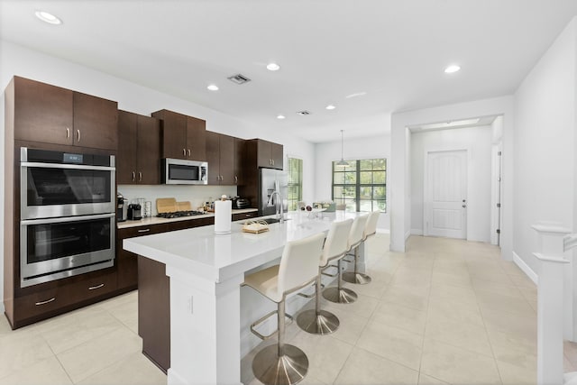 kitchen featuring visible vents, an island with sink, light countertops, stainless steel appliances, and a sink