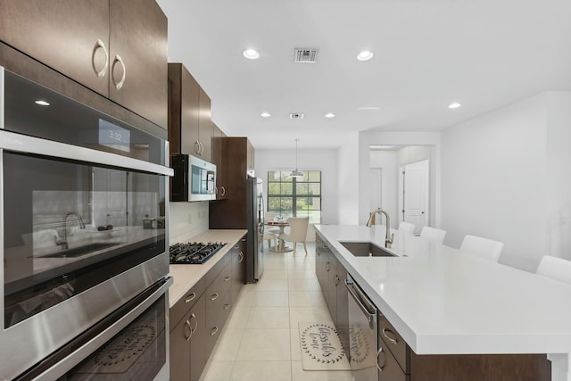 kitchen with visible vents, a center island with sink, a sink, stainless steel appliances, and light countertops