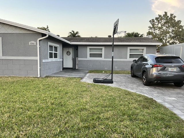 single story home featuring roof with shingles, concrete block siding, and a front yard