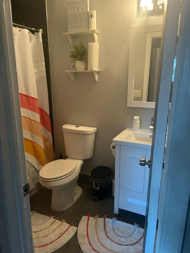 bathroom with curtained shower, toilet, wood finished floors, vanity, and baseboards