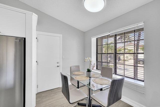 dining room with light wood-style floors, lofted ceiling, a textured ceiling, and baseboards