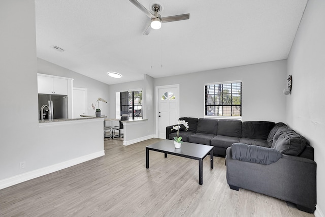 living area featuring vaulted ceiling, light wood finished floors, visible vents, and baseboards