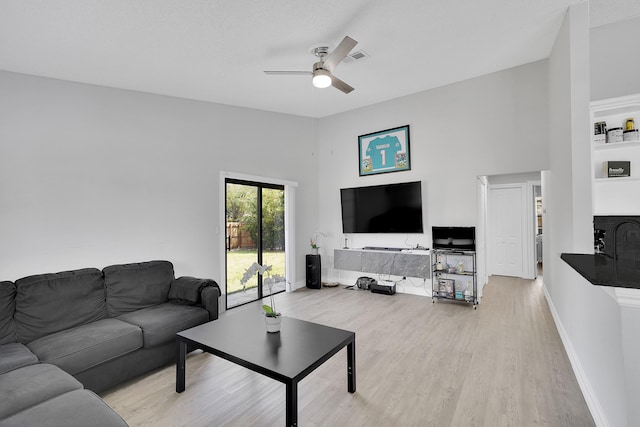 living area featuring a towering ceiling, light wood-style floors, baseboards, and a ceiling fan