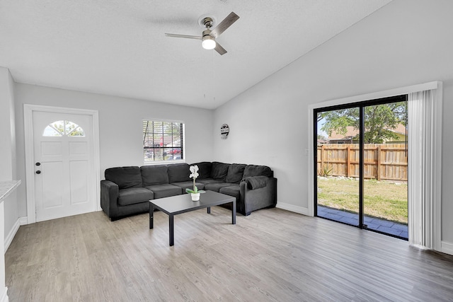 living area featuring a textured ceiling, wood finished floors, a ceiling fan, baseboards, and vaulted ceiling