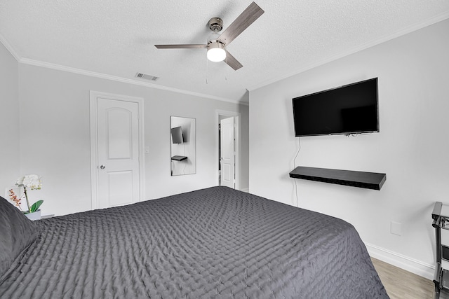 bedroom with a textured ceiling, ornamental molding, wood finished floors, and visible vents