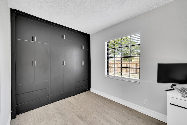 unfurnished bedroom featuring light wood-style flooring, a closet, baseboards, and a textured ceiling