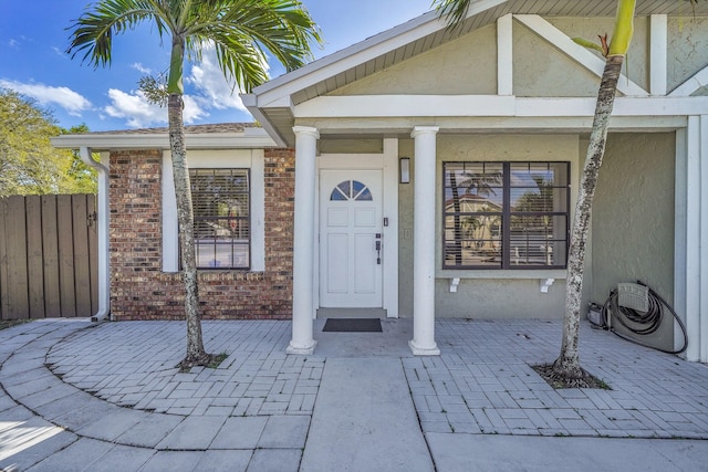 doorway to property featuring a porch, brick siding, fence, and stucco siding