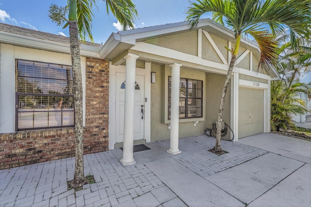 property entrance with a garage, concrete driveway, brick siding, and stucco siding