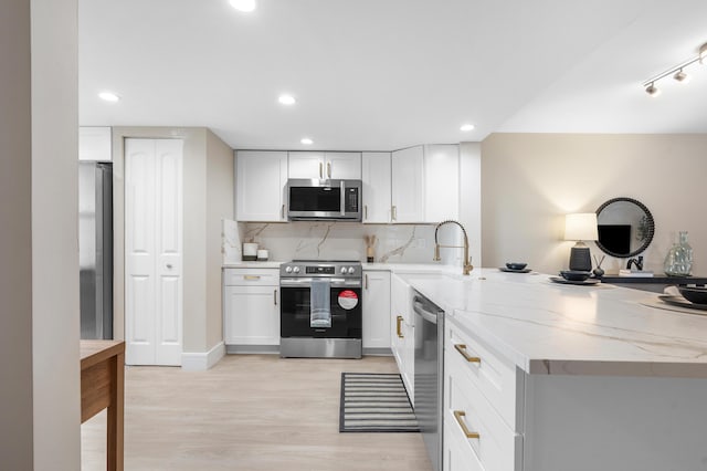 kitchen with light stone counters, light wood-style flooring, a peninsula, appliances with stainless steel finishes, and decorative backsplash