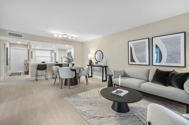 living room featuring light wood-type flooring, visible vents, and baseboards