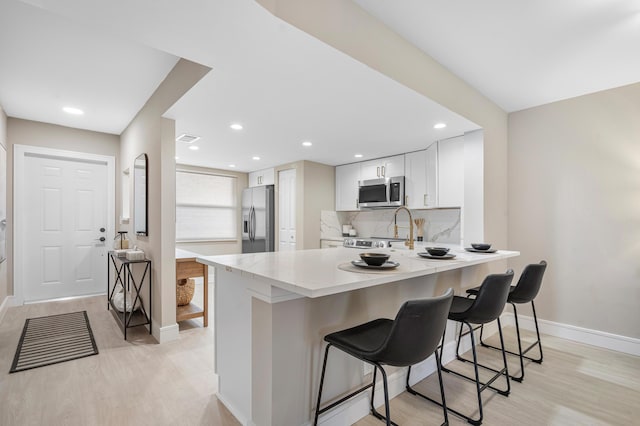 kitchen with stainless steel appliances, decorative backsplash, white cabinets, a peninsula, and a kitchen breakfast bar