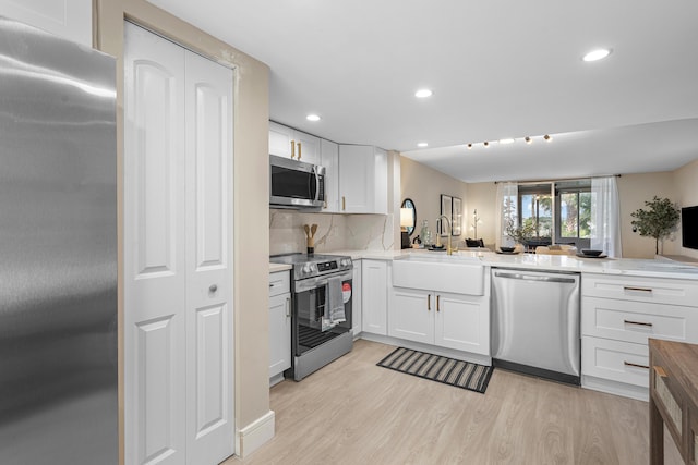 kitchen with light wood finished floors, white cabinetry, appliances with stainless steel finishes, and a sink