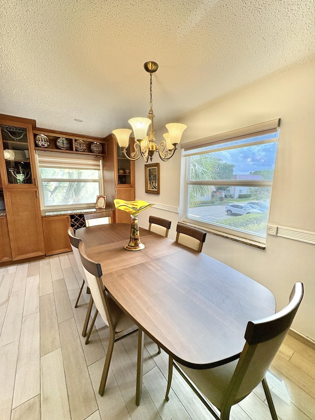 dining space featuring light wood-type flooring, a chandelier, and a textured ceiling