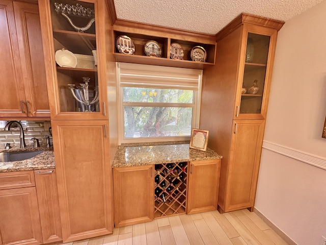 bar featuring light wood-style floors, a textured ceiling, baseboards, and a sink