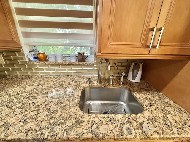 details featuring light stone counters, a sink, and backsplash