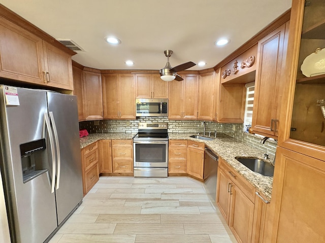 kitchen with appliances with stainless steel finishes, a sink, and light stone counters