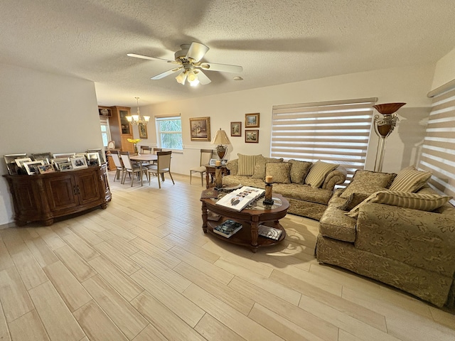 living room with ceiling fan with notable chandelier, light wood finished floors, and a textured ceiling