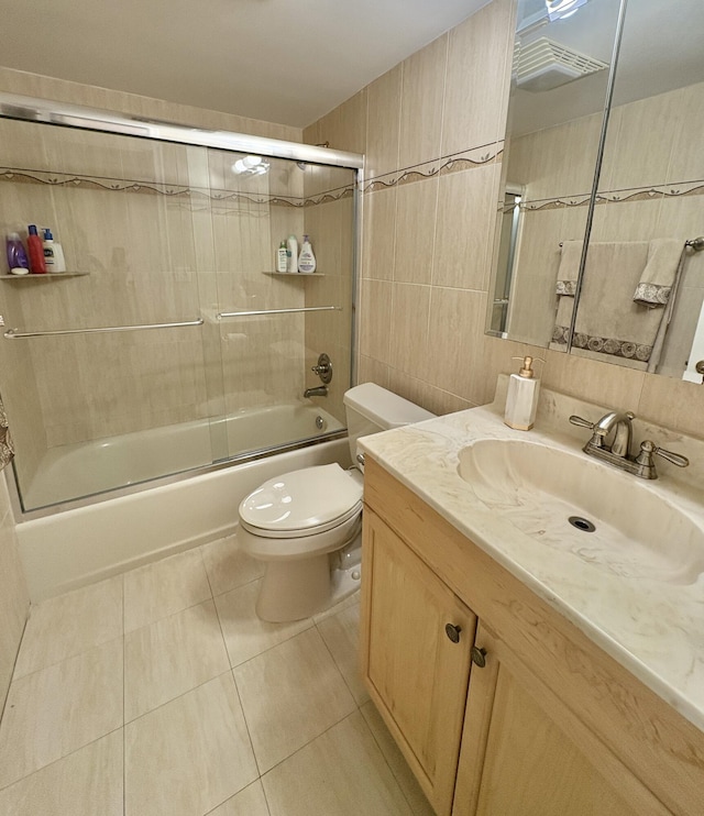 full bath with toilet, shower / bath combination with glass door, tile patterned flooring, vanity, and tile walls