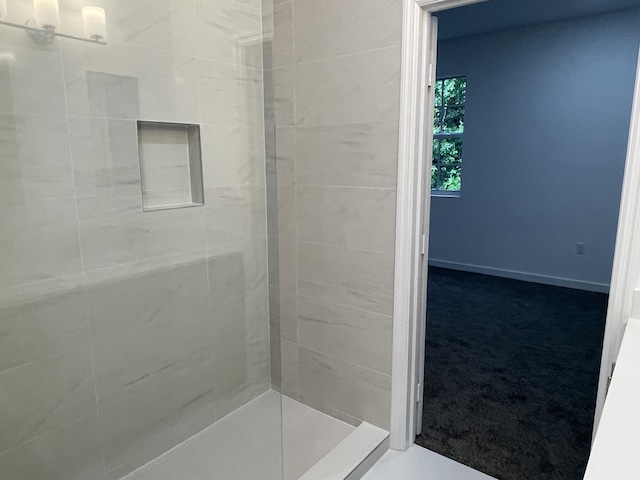 bathroom with a tile shower and baseboards