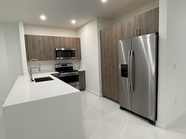 kitchen featuring light countertops, appliances with stainless steel finishes, brown cabinetry, modern cabinets, and a sink