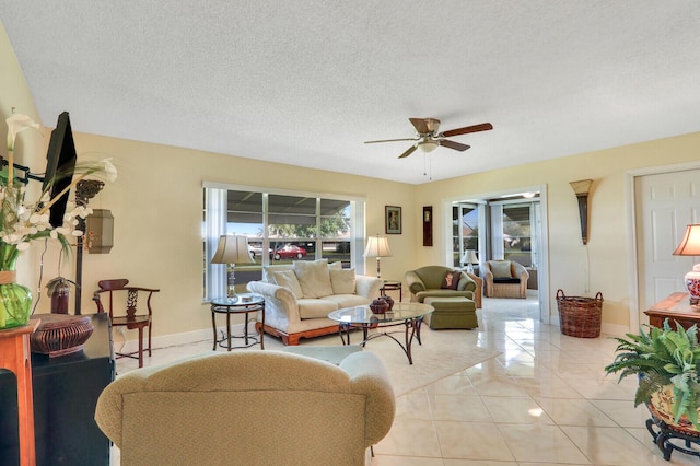 living room featuring ceiling fan, a textured ceiling, baseboards, and light tile patterned floors