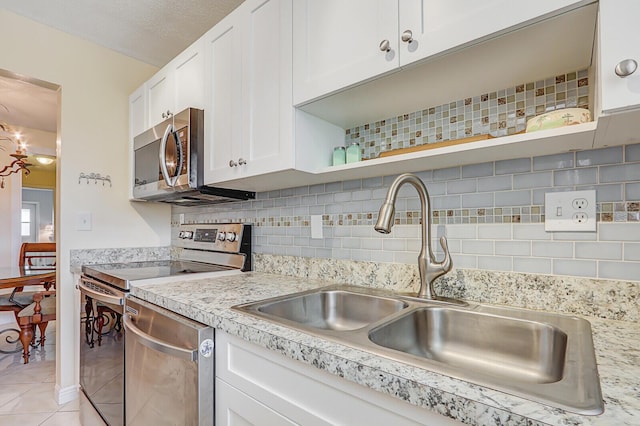 kitchen with stainless steel appliances, tasteful backsplash, light countertops, white cabinets, and a sink