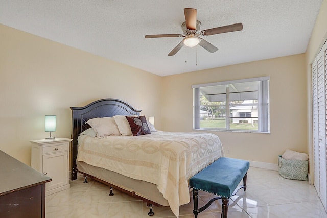 bedroom with a textured ceiling, light tile patterned flooring, a ceiling fan, and baseboards