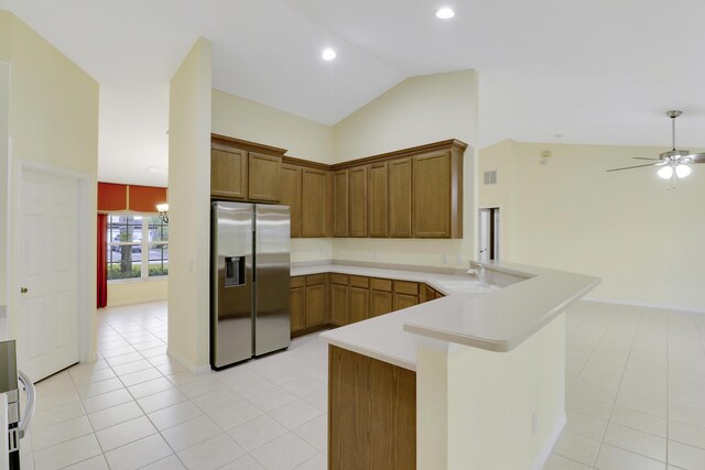 kitchen featuring stainless steel refrigerator with ice dispenser, light countertops, brown cabinetry, a sink, and a peninsula