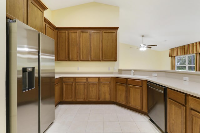 kitchen with a sink, vaulted ceiling, light countertops, appliances with stainless steel finishes, and brown cabinetry