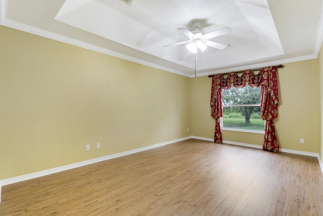 empty room with a tray ceiling, crown molding, light wood-style flooring, a ceiling fan, and baseboards