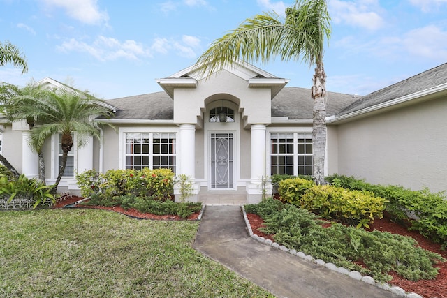 view of exterior entry featuring a shingled roof, a lawn, and stucco siding