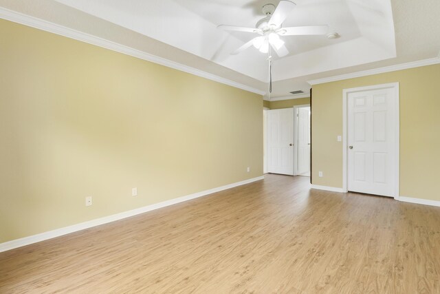 unfurnished room with a ceiling fan, baseboards, light wood-type flooring, a tray ceiling, and crown molding