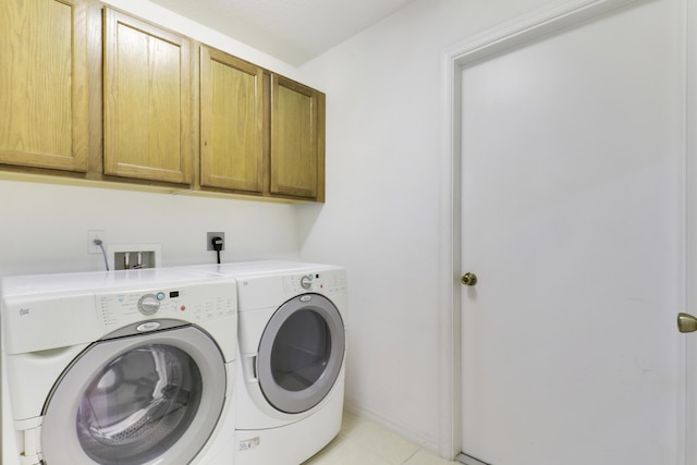 clothes washing area featuring light tile patterned flooring, washing machine and clothes dryer, and cabinet space