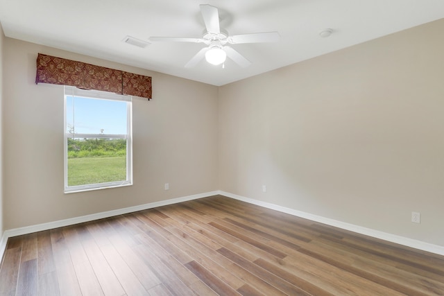 spare room with wood finished floors, visible vents, and baseboards