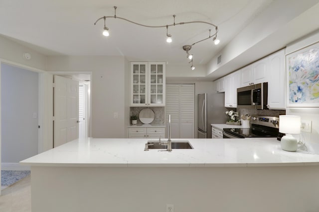 kitchen featuring decorative backsplash, appliances with stainless steel finishes, a peninsula, glass insert cabinets, and light stone countertops