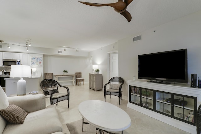 living room with light tile patterned floors, a ceiling fan, visible vents, and a textured ceiling